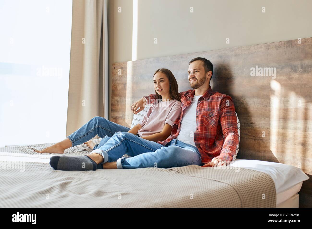 Beautiful young couple sit hugging on bed, watching attentively TV, focus in device, looking