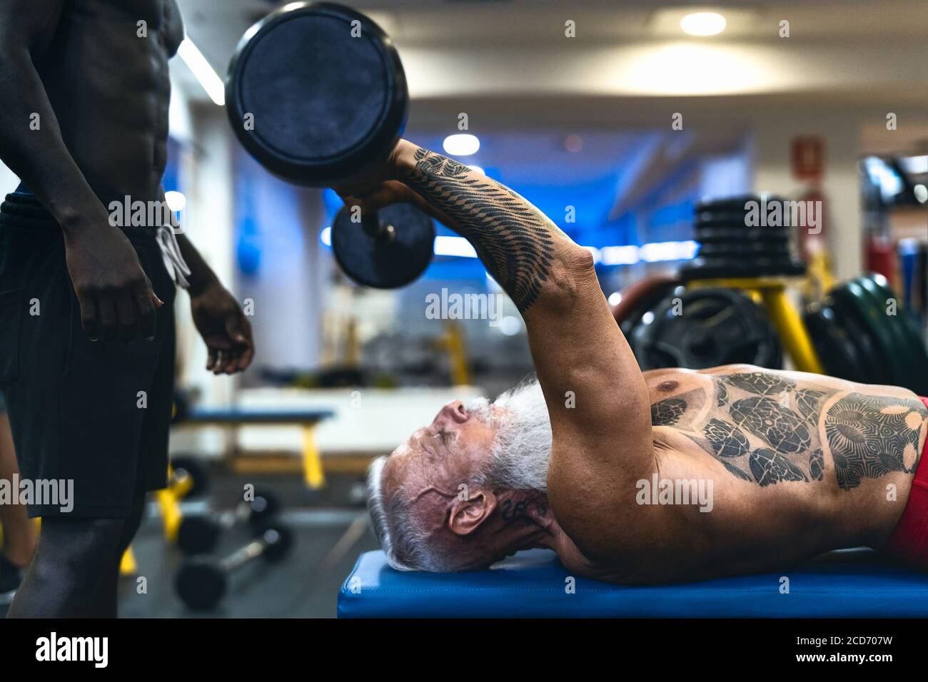 Senior fit man weight lifting with personal trainer in gym sport club - Mature bodybuilder doing workout session Stock Photo