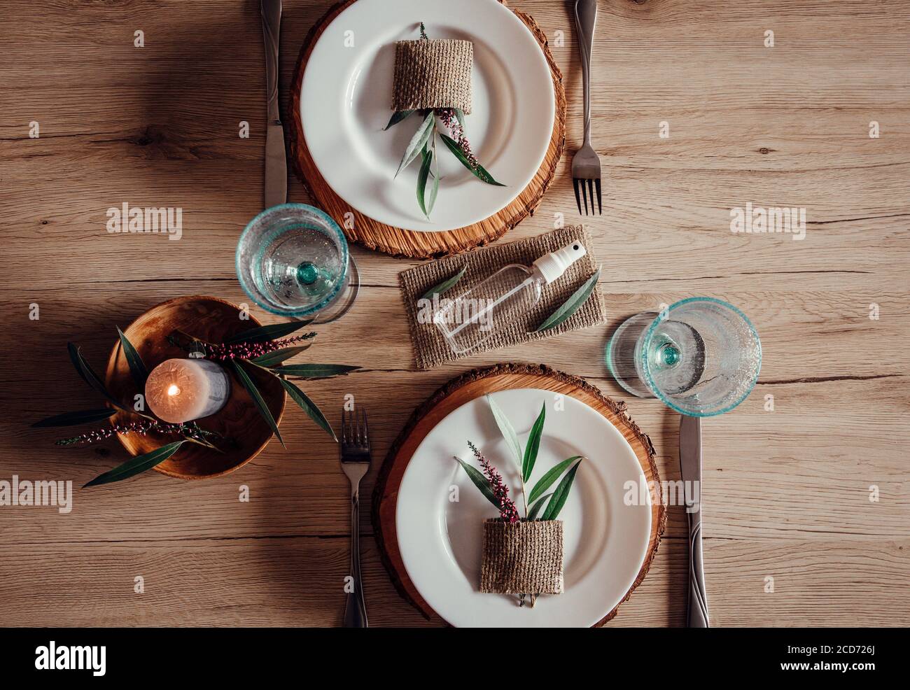 Restaurant table set with hand sanitizer bottle in center. White plates with leaf and heather flower decoration.Virus spreading prevention. Stock Photo