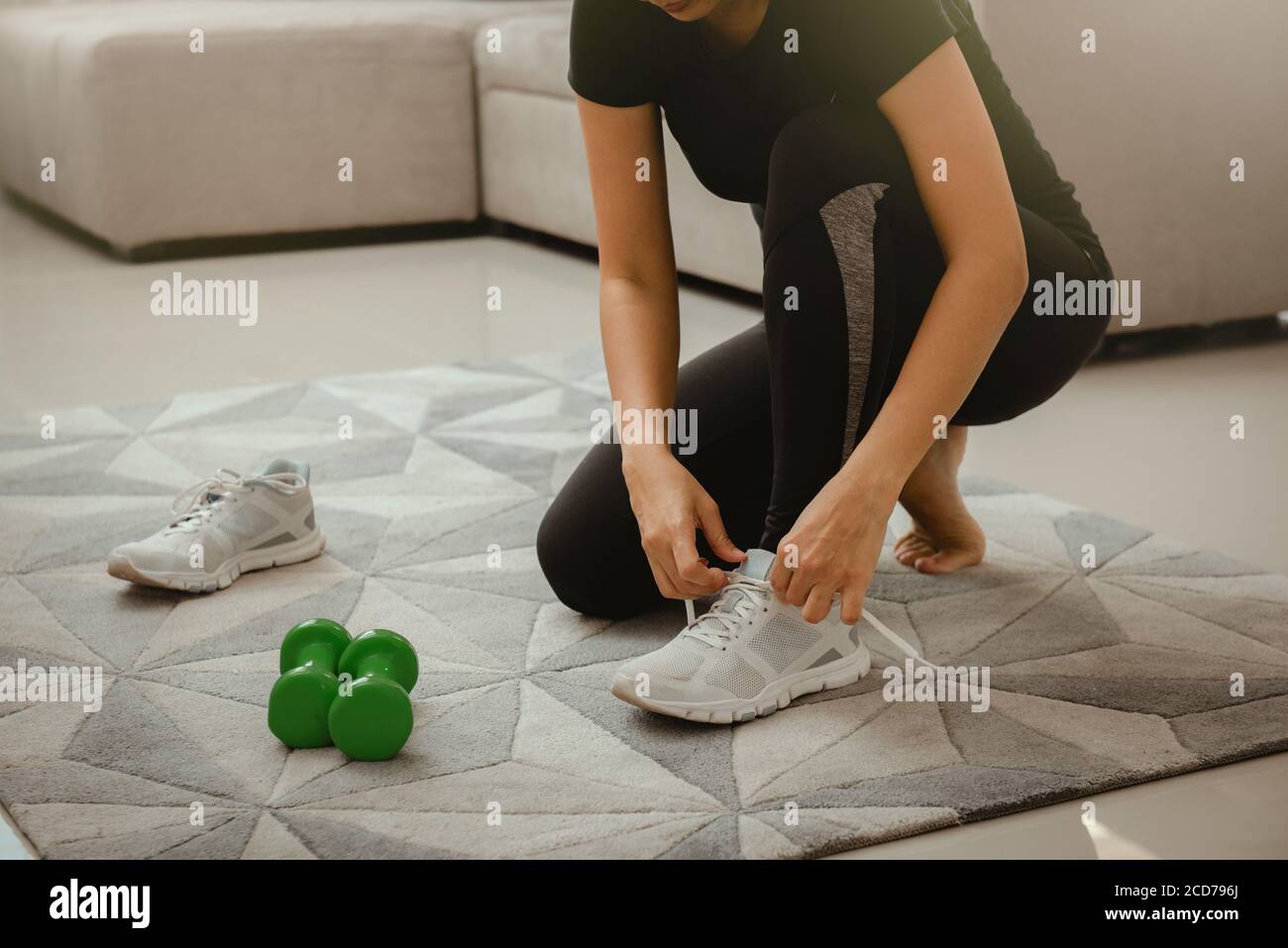 Woman getting ready for workout at home. She is tying shoelace on sneakers. Sport and recreation concept. Stock Photo