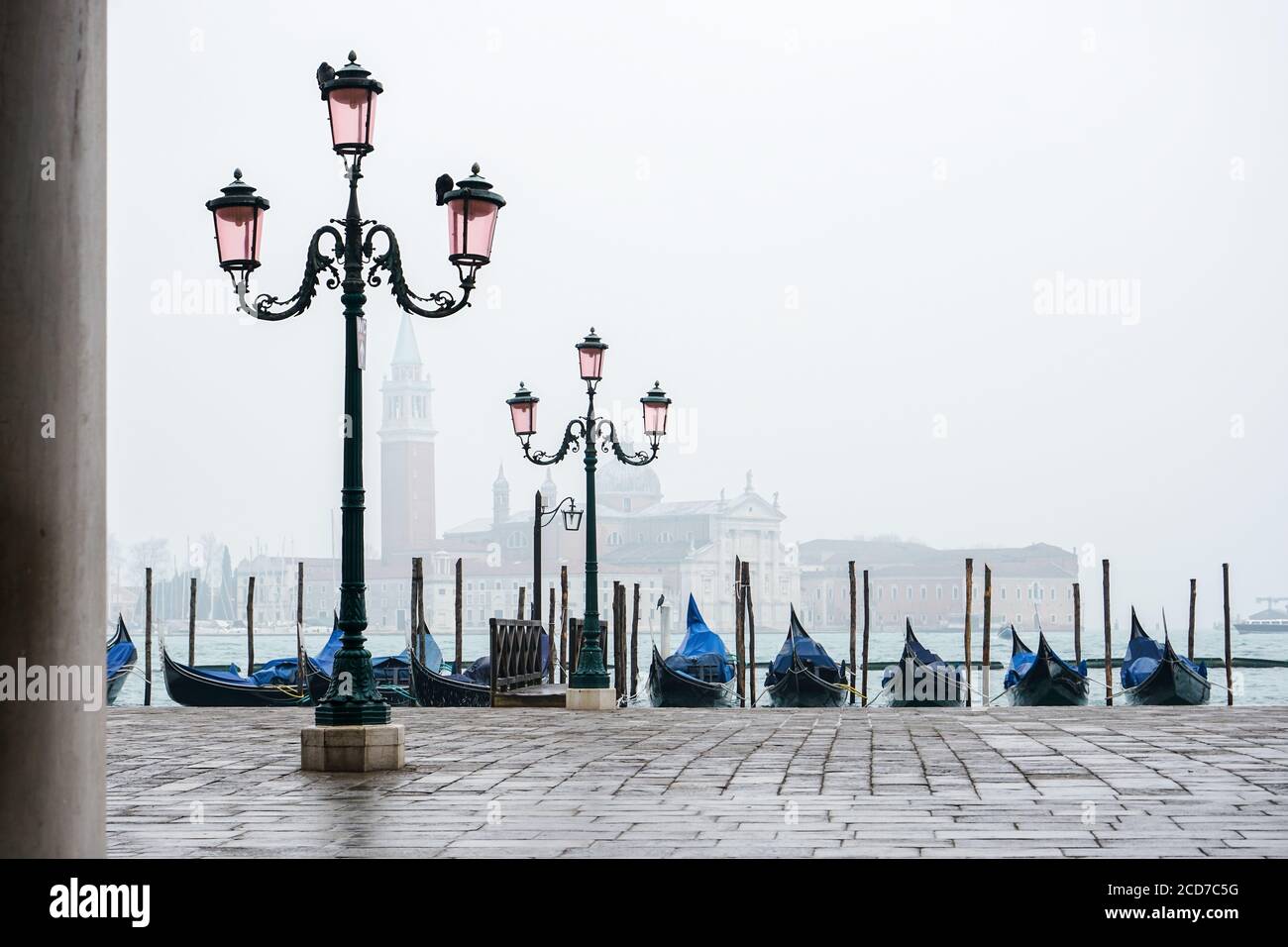 Romantic promenade in Venice with street lamps and blue gondolas docked in the grand canal, during a foggy day. Stock Photo