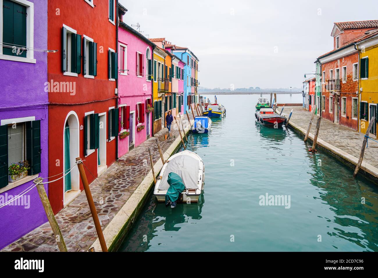 Venice, Italy - January 2020: Colorful houses in Burano Island along quaint canal with boats docked at riverside Stock Photo