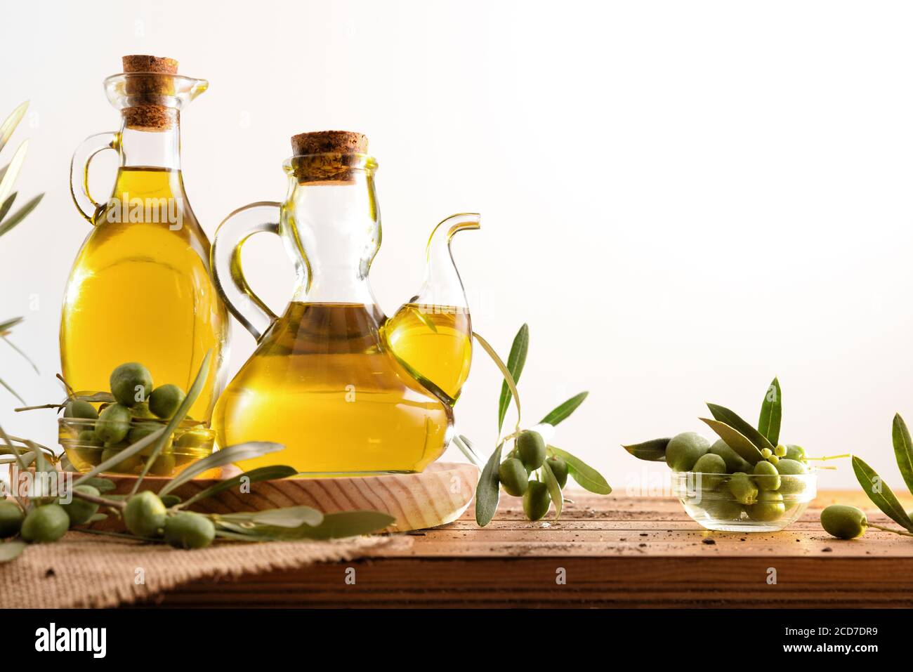 Olive oil dispensers on wooden table with raw olives and leaves with