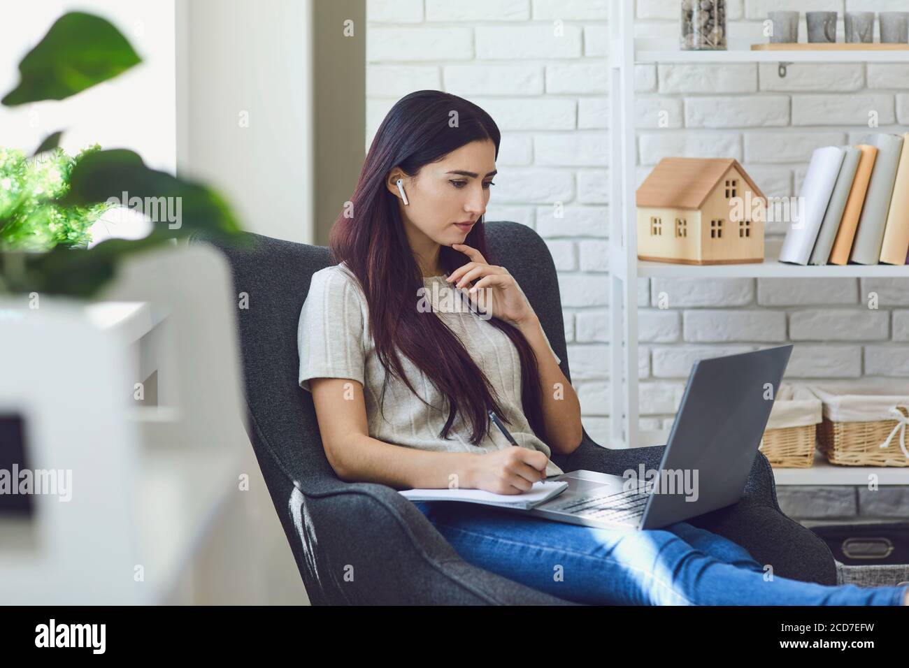 Female freelancer in earbuds watching laptop during work at home Stock ...