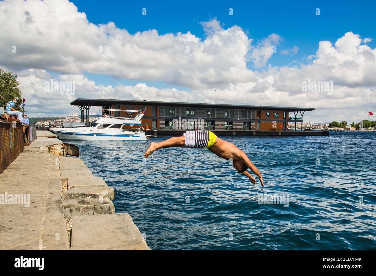 ISTANBUL / TURKEY - 07.17.2020: Young turkish man jumping in the sea from the pier of Karakoy on a hot summer day, the Golden Horn, Istanbul, Turkey. Stock Photo