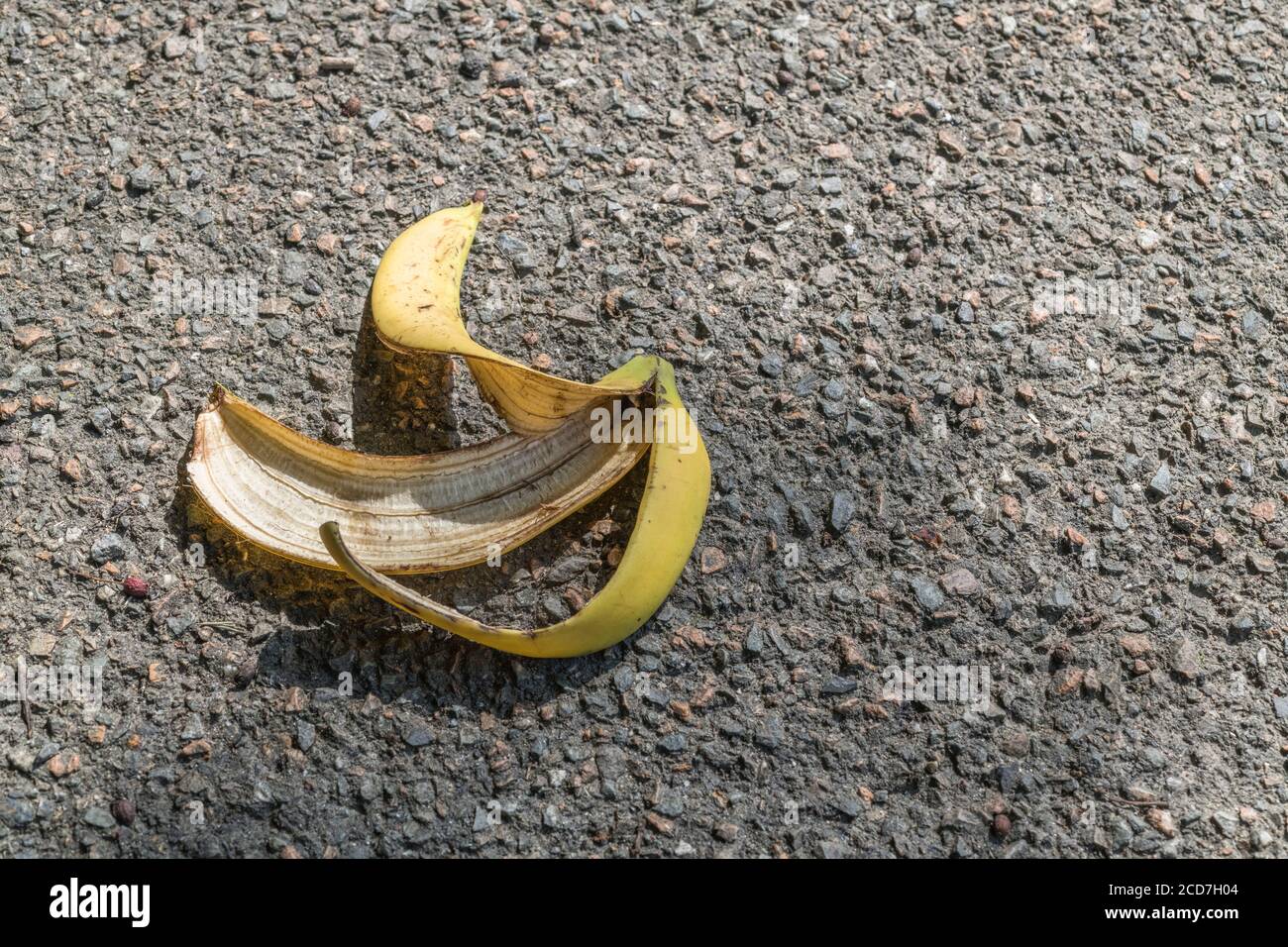 Discarded banana skin / banana peel left on asphalt footpath / pavement, with slight shadow from overhead tree branch. For slip-up, faux pas, blunder. Stock Photo