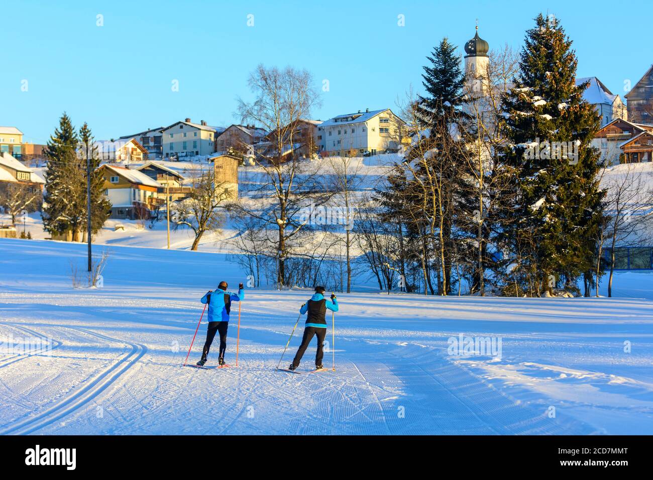 Two skiers doing a skating exercise in late winter afternoon near a village Stock Photo