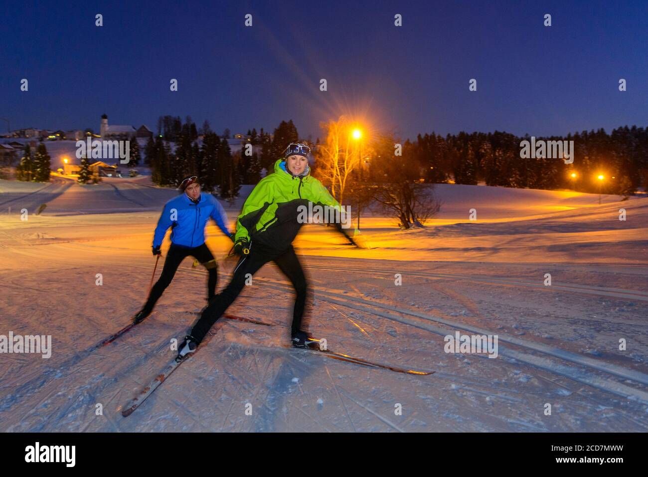 Two skiers doing a skating exercise on winter evening on floodlight slopes Stock Photo