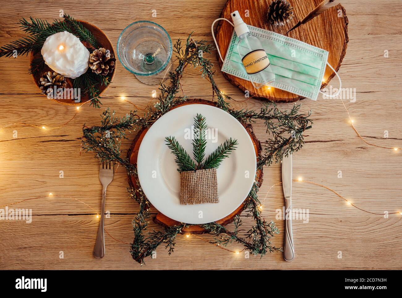 Christmas eve holiday party decorated table set with disposable medical mask and alcohol hand sanitizer bottle. Coronavirus (Covid 19) spreading. Stock Photo
