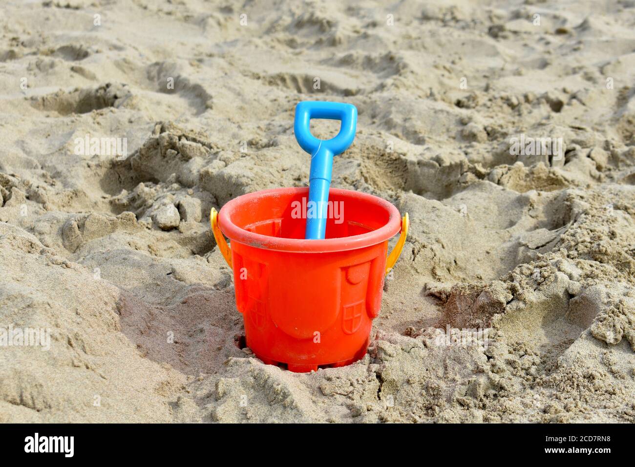 close up of pink plastic sand castle bucket with blue spade on sand