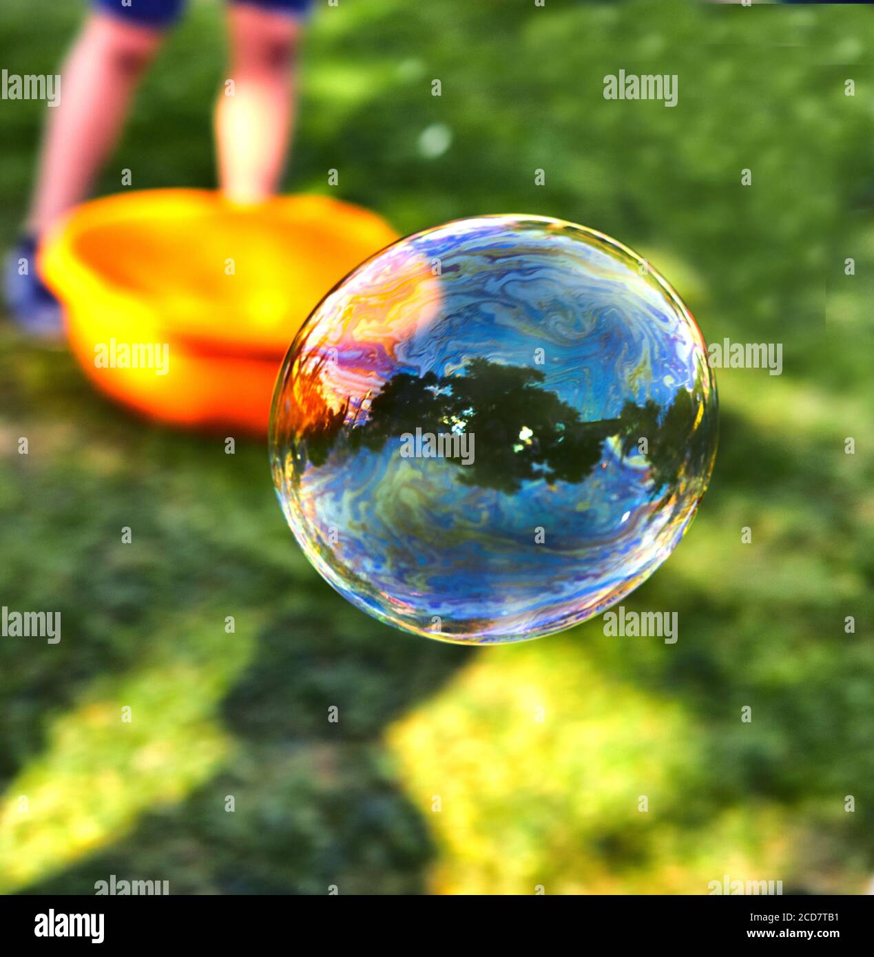 A soap bubble flies against the background of green grass. Bubbles of air on a sunny summer day outdoors. Stock Photo