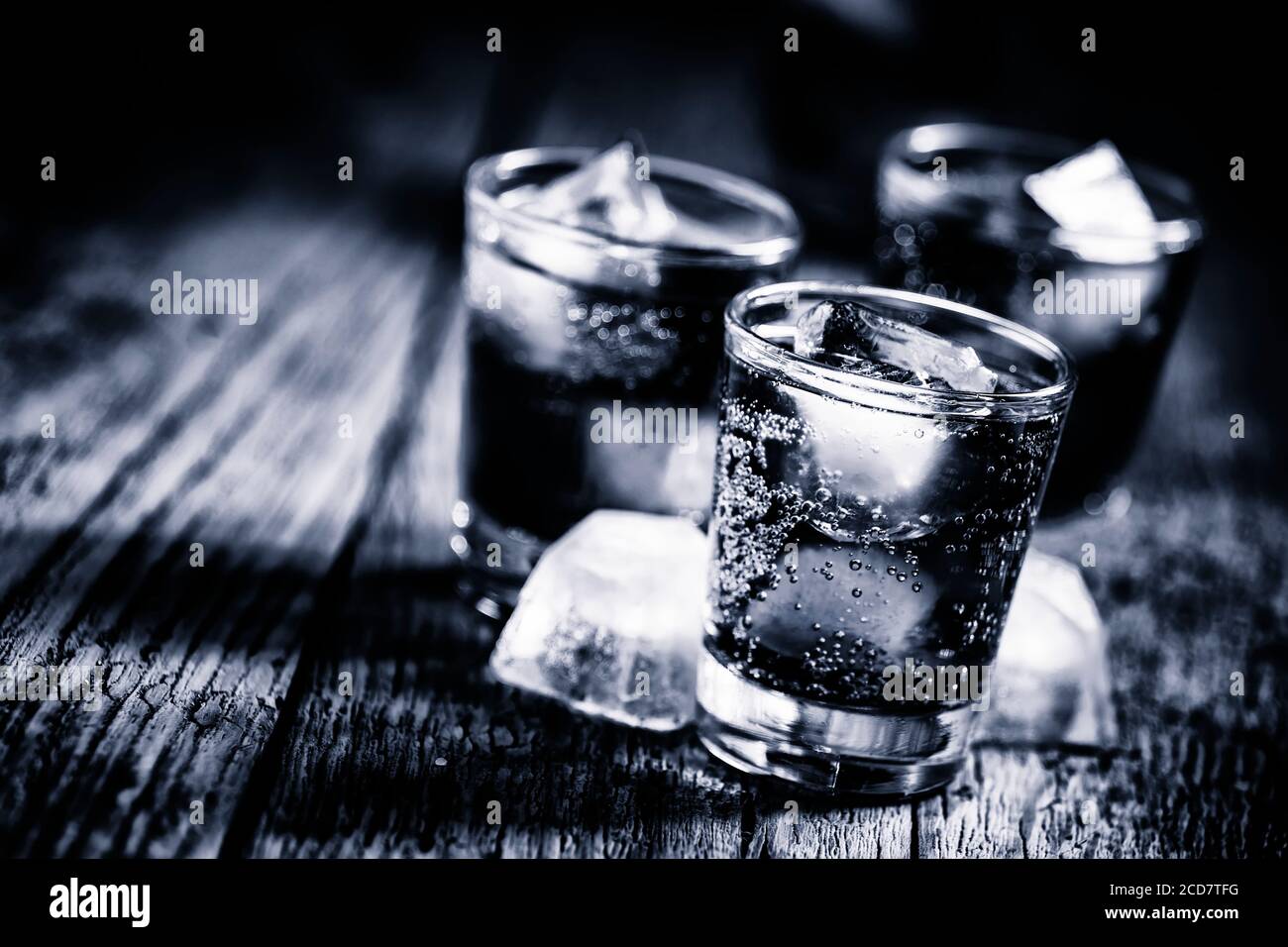 Black and white photo. Alcoholic cocktail from cola with whiskey and ice cubes,  wooden background, selective focus Stock Photo