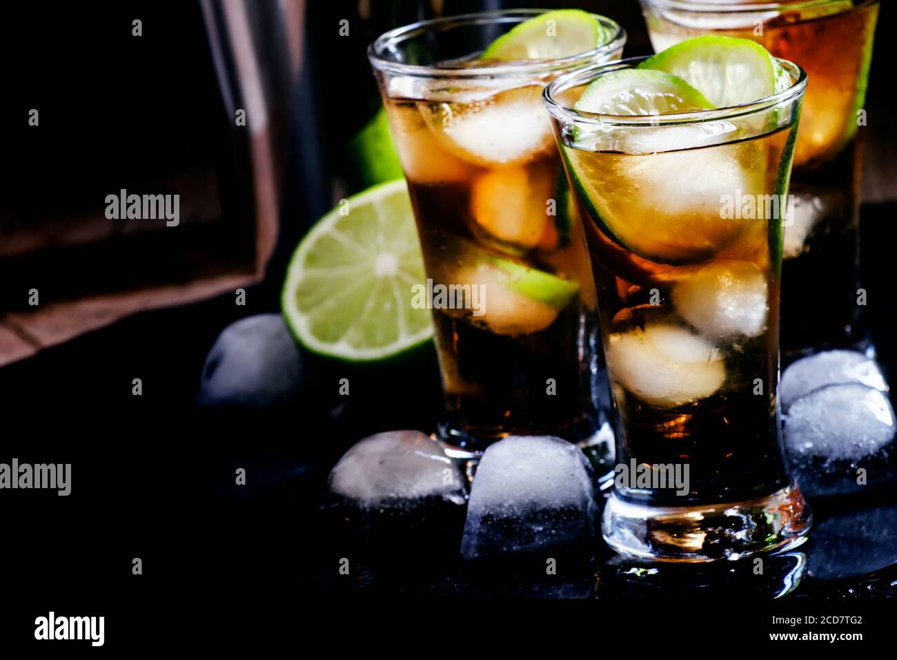 Alcoholic cocktail spiced rum with cola, lime and ice cubes, shaker, black background, selective focus Stock Photo