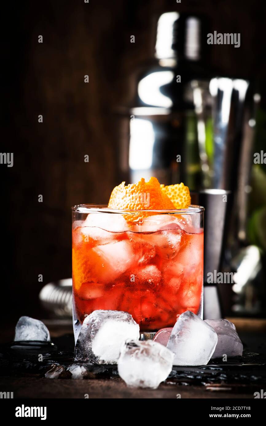 Americano Alcohol cocktail with red vermouth, bitter, soda, orange zest and ice, dark wooden bar counter background, bar tools, selective focus Stock Photo