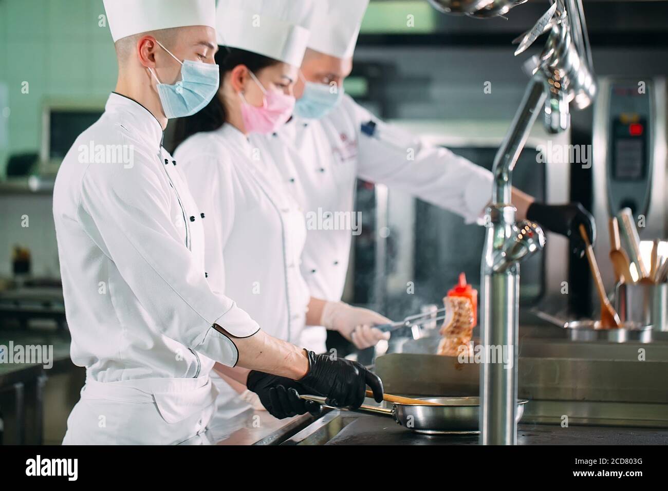 Chefs in protective masks and gloves prepare food in the kitchen of a
