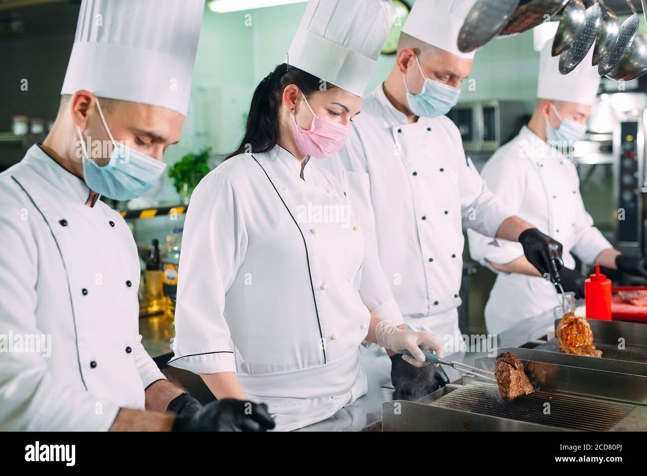 Chefs in protective masks and gloves prepare food in the kitchen of a restaurant or hotel Stock