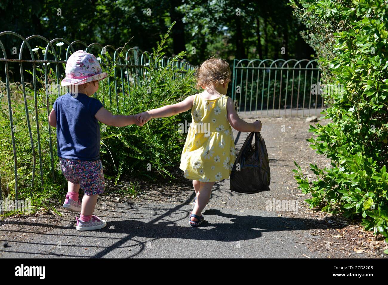 Two young children holding hands and walking away down a footpath in summer clothes and sunshine Stock Photo