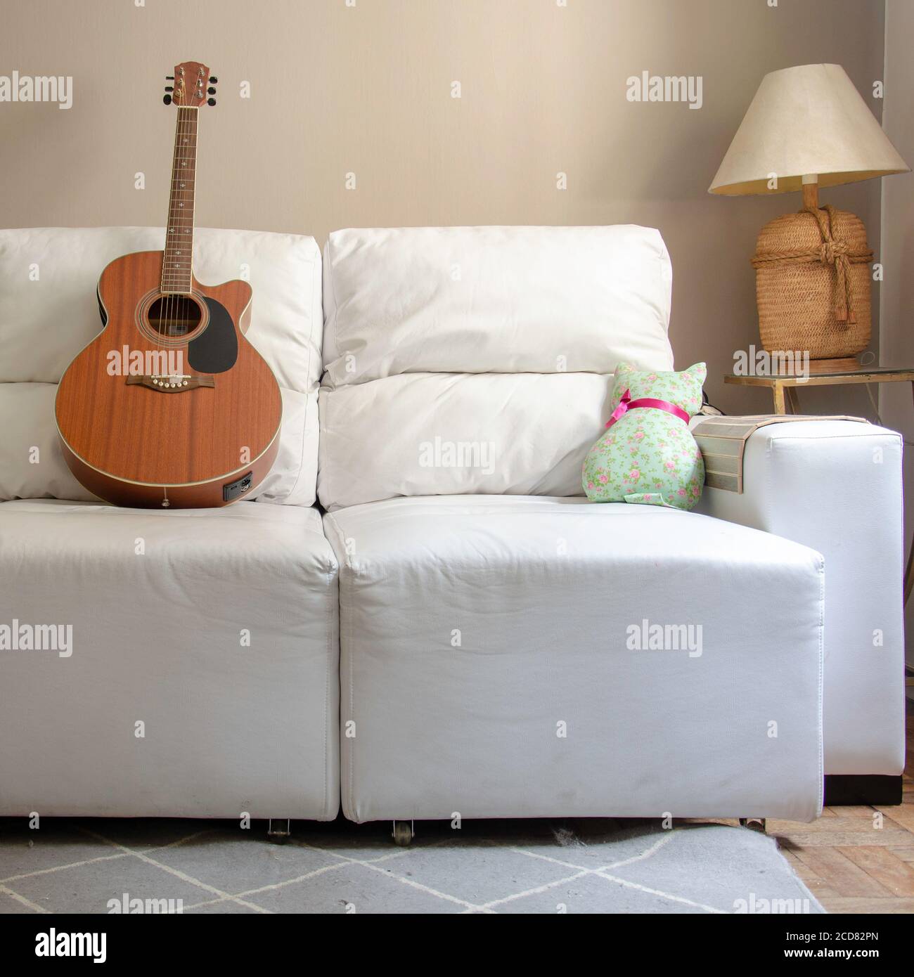 Home decor: living room with wooden guitar over a white sofa and lamp on side table with light brown background wall Stock Photo