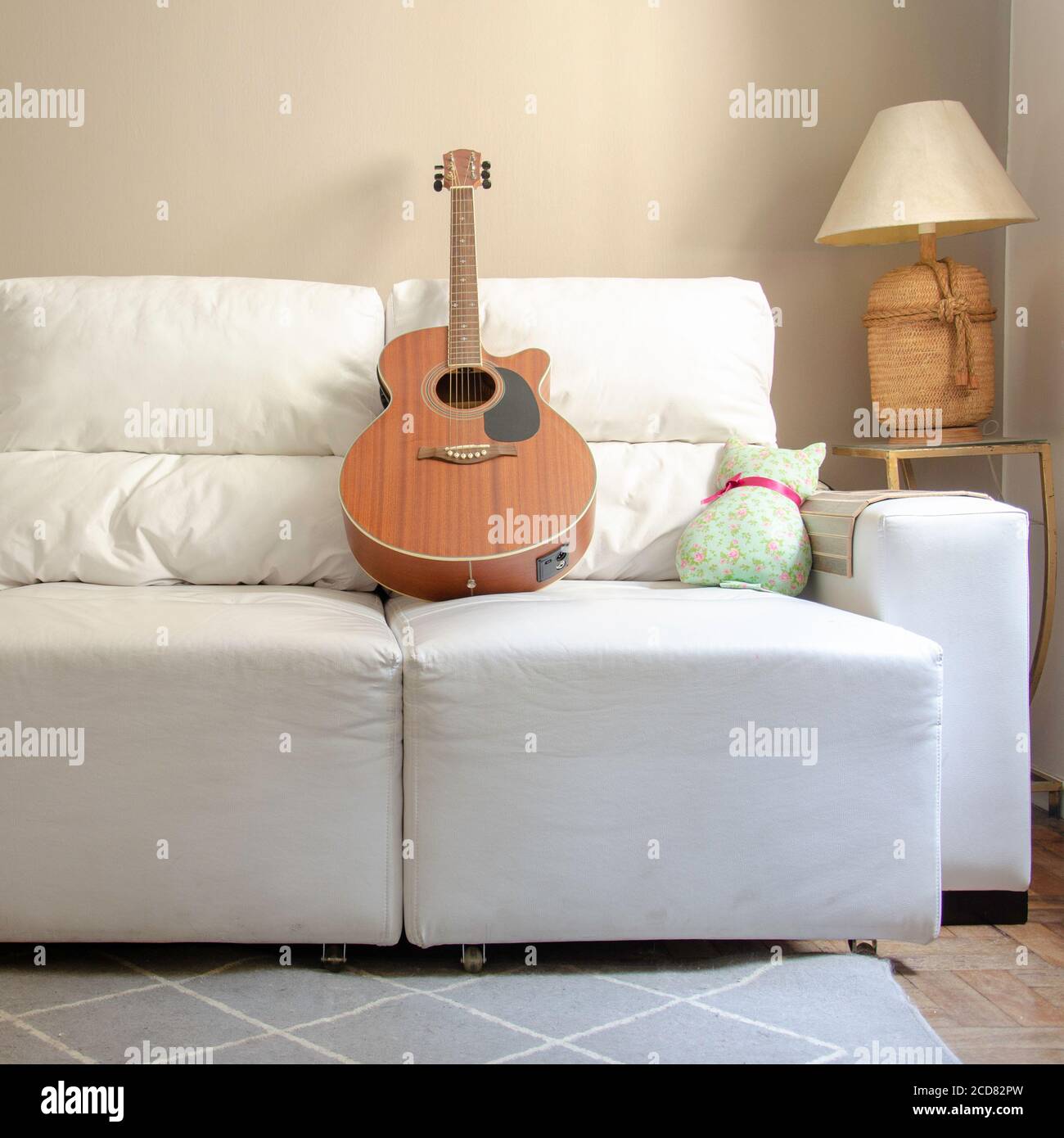 Home decor: living room with wooden guitar over a white sofa and lamp on side table with light brown background wall Stock Photo