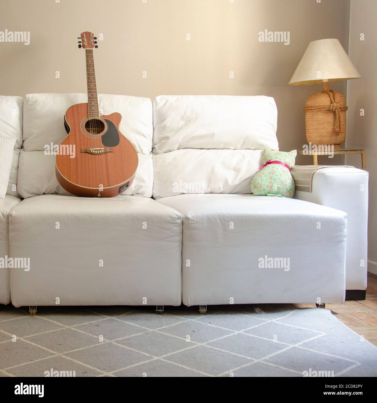 Home decor: living room with wooden guitar over a white sofa and lamp on side table with light brown background wall Stock Photo