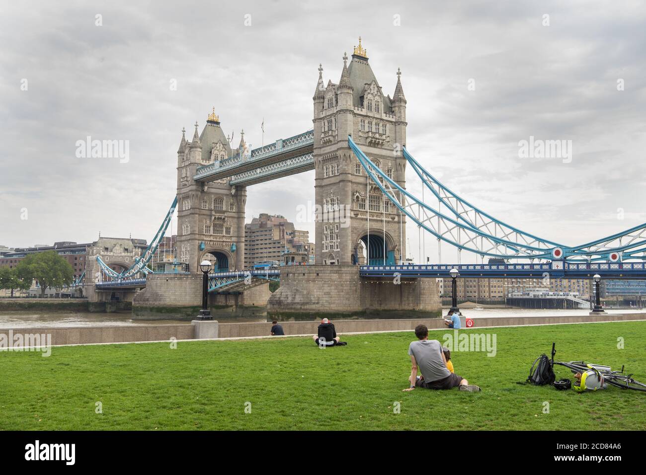 People relaxing in front of Tower Bridge on a cloudy day. London Stock