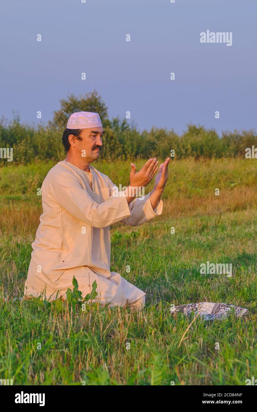 A muslim senior man wearing a skullcap and traditional clothes prays Portrait of a cute young black bull on a pasture Stock Photo
