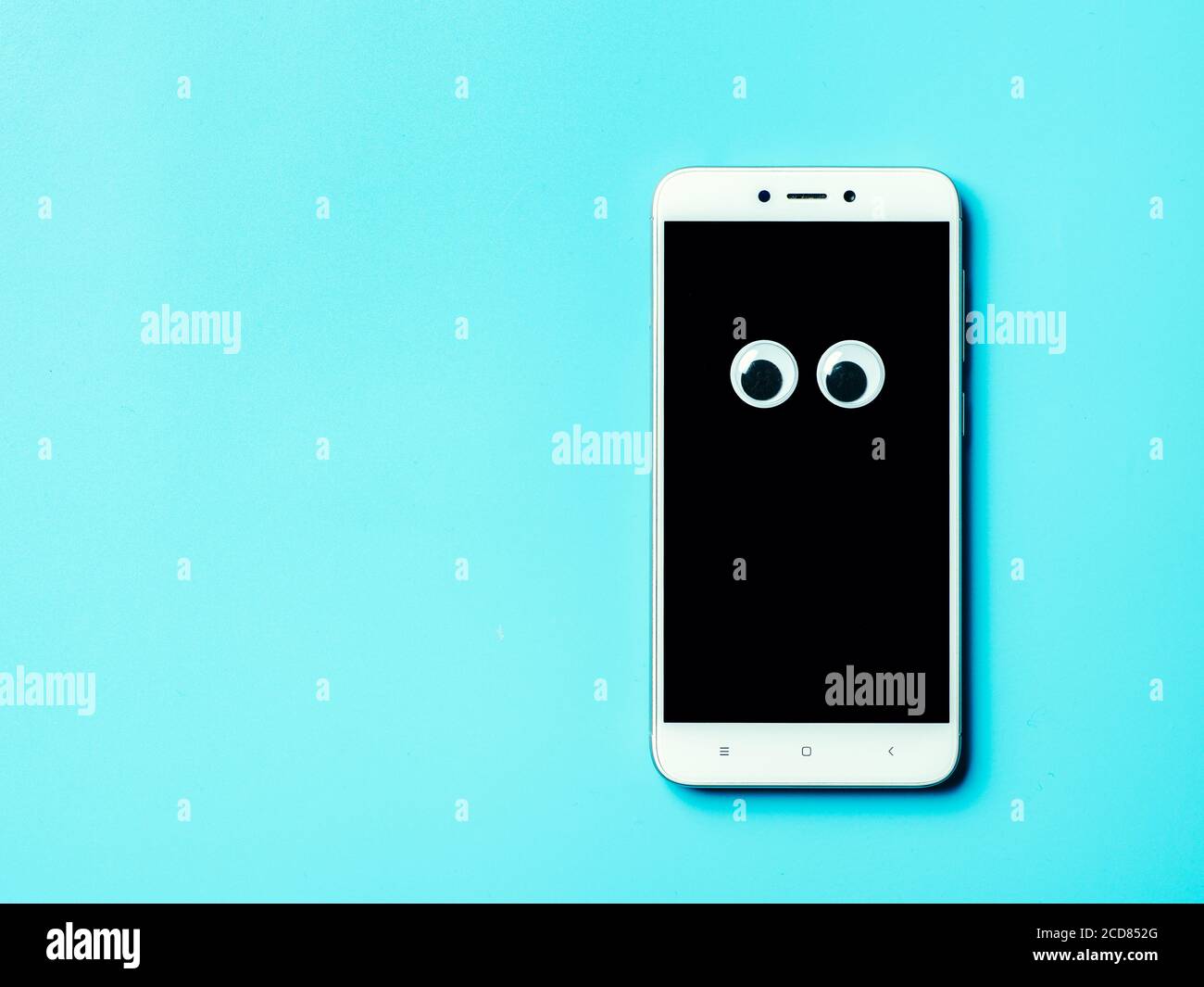 googly eyes on smartphone screen over blue background with copy space