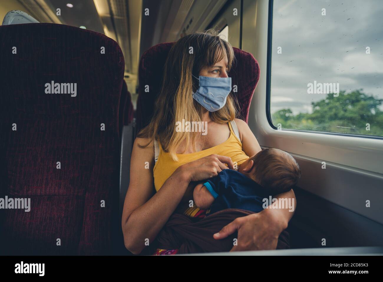 A young mother wearing a face mask is breastfeeding her baby on a train