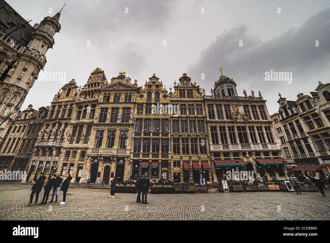 People standing by an opulent building facade or exterior in the noble Bruxelles Grand Place with its both Gothic and Baroque architecture - Brussels Stock Photo