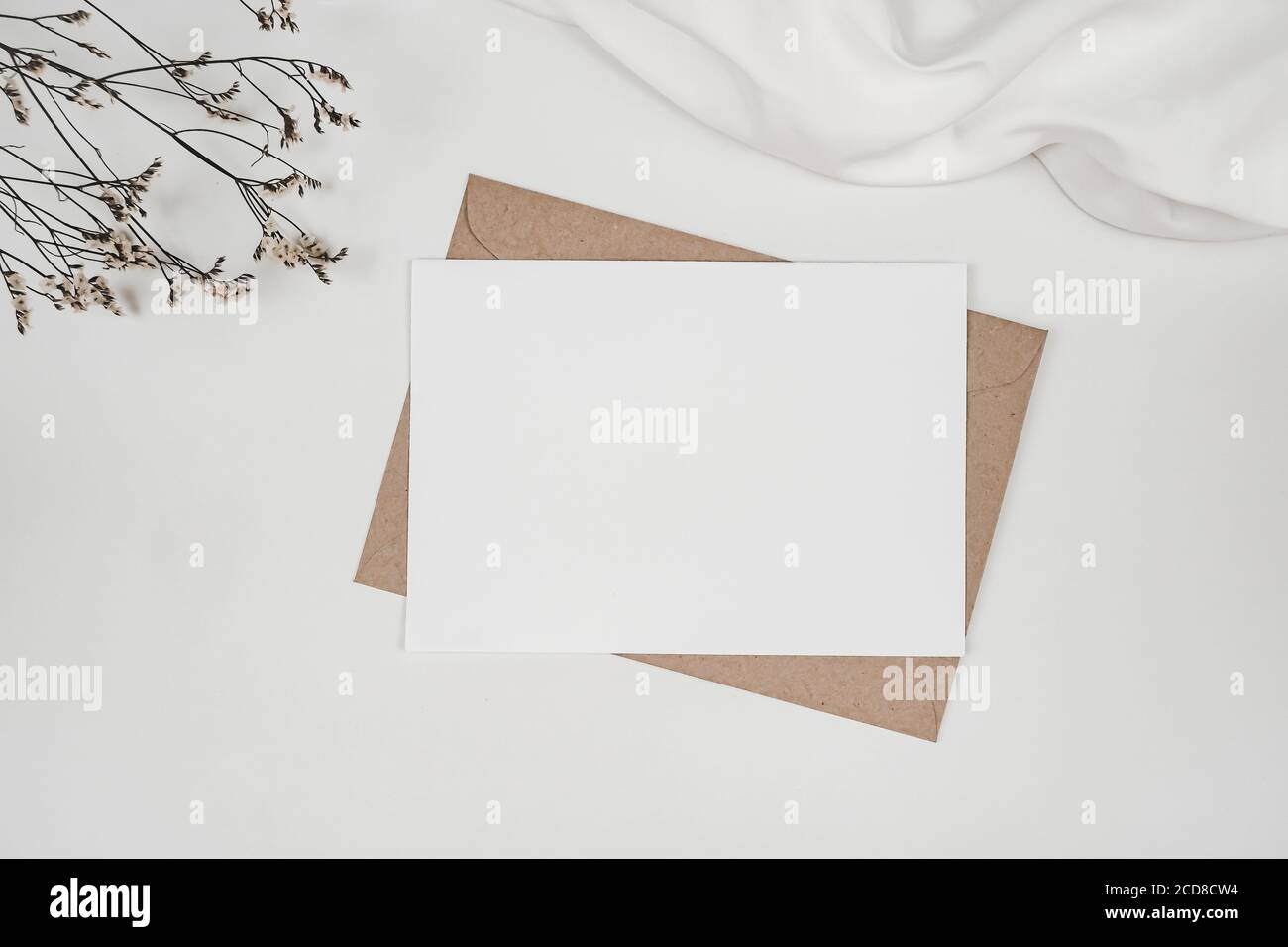 Blank white paper on brown paper envelope with Limonium dry flower and white cloth. Mock-up of horizontal blank greeting card. Top view of Craft envel Stock Photo