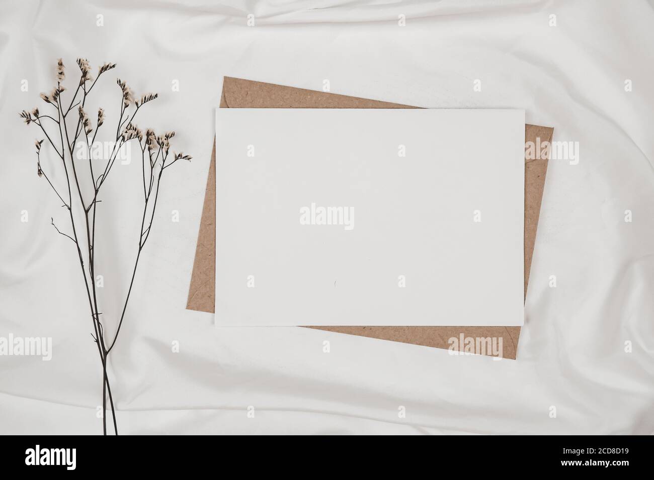 Blank white paper on brown paper envelope with Limonium dry flower on white cloth. Mock-up of horizontal blank greeting card. Top view of Craft envelo Stock Photo