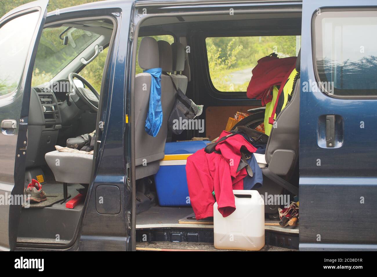 Looking into the open door of a mini van filled with holiday, staycation, items including water container, cool box,coats, shoes and umbrellas Stock Photo
