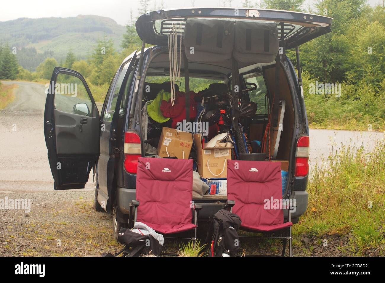 Looking into the open door of a mini van filled with holiday, staycation, items including water container, cool box,coats, shoes and umbrellas Stock Photo