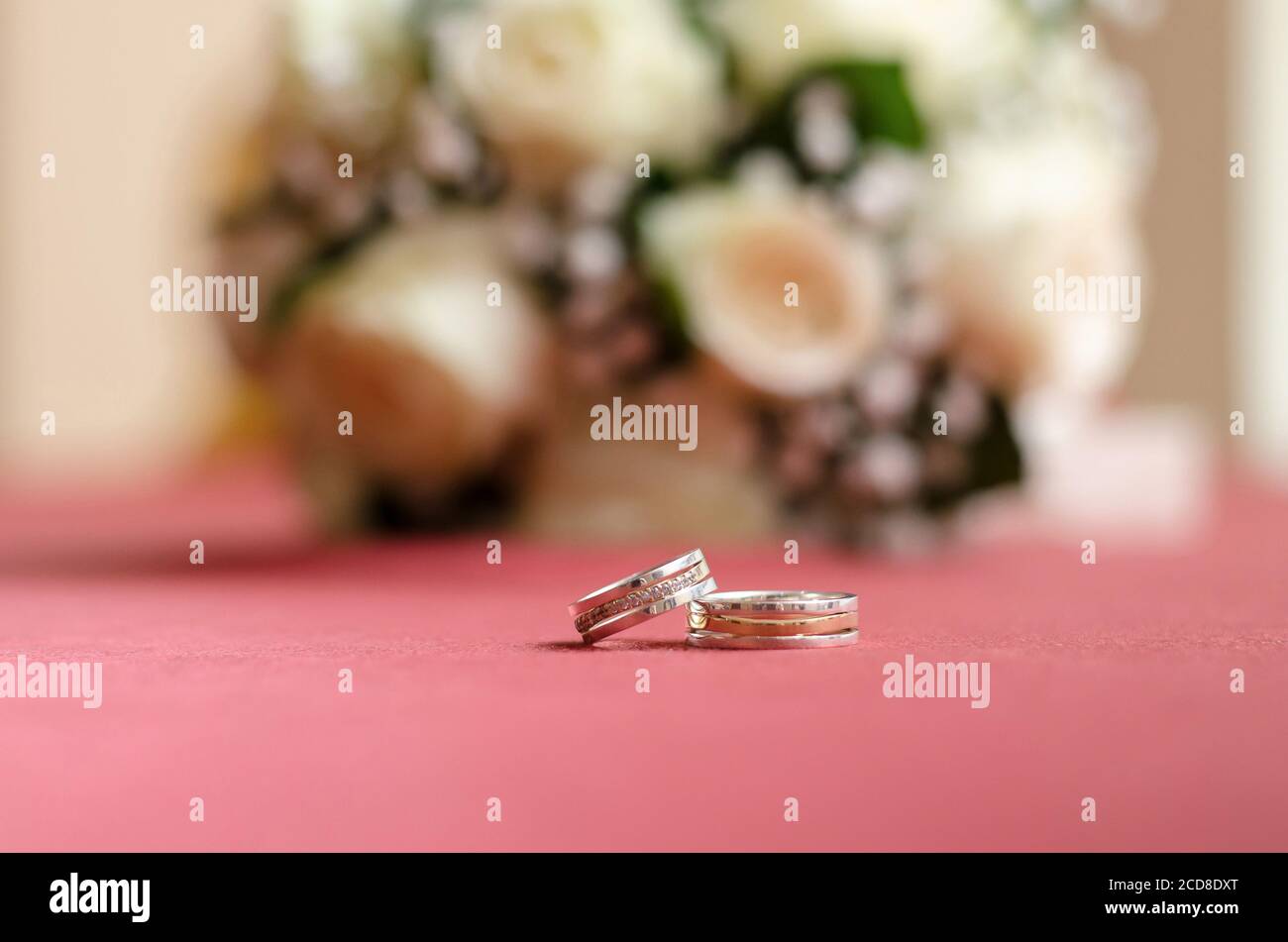 Wedding rings on a pink table, on the background of a bouquet of flowers. Close up Stock Photo