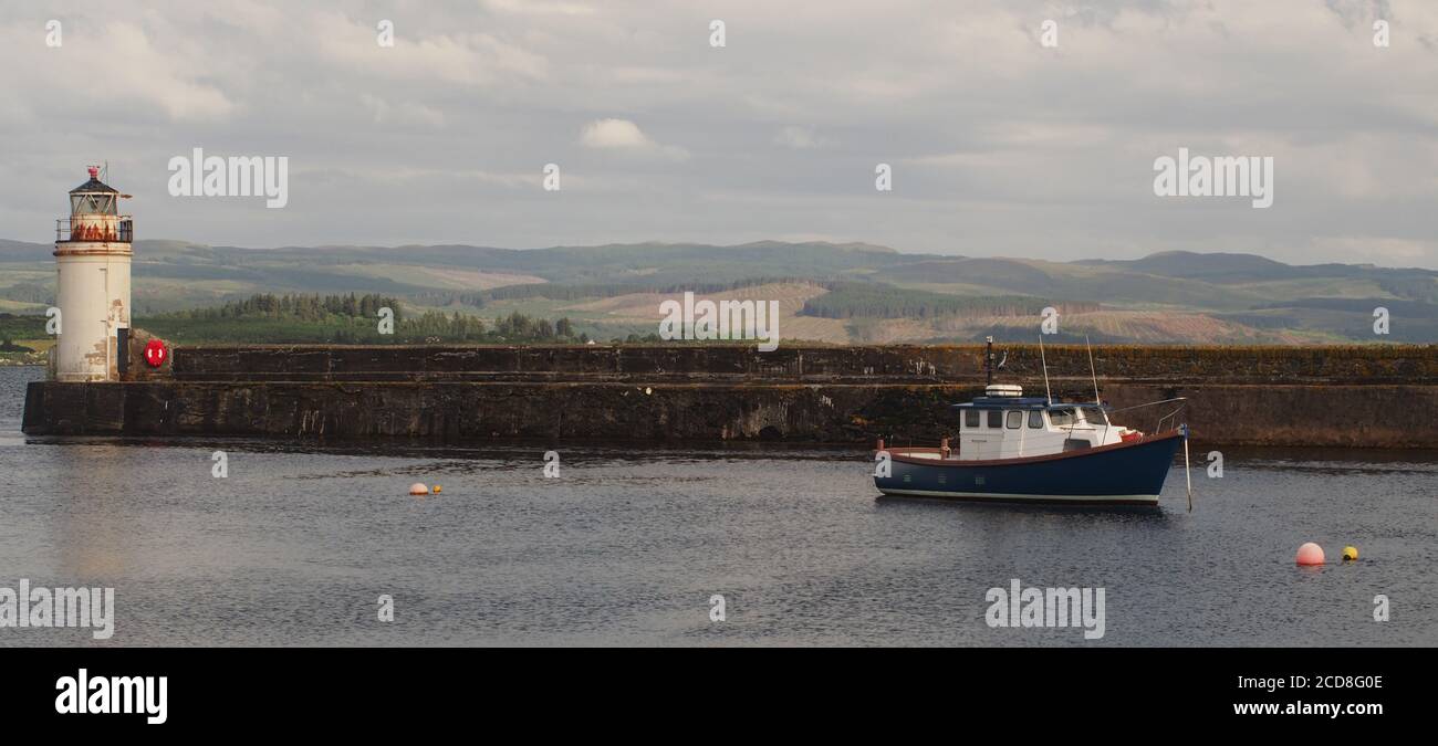 A view of Ardrishaig pier, Argyll, Scotland with the lighthouse on the end and a small fishing boat moored in the calm waters Stock Photo