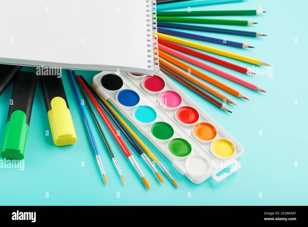 An album for creative development at school, with stationery on a cyanide background. A palette of colored paints, markers, brushes and pencils. Stock Photo
