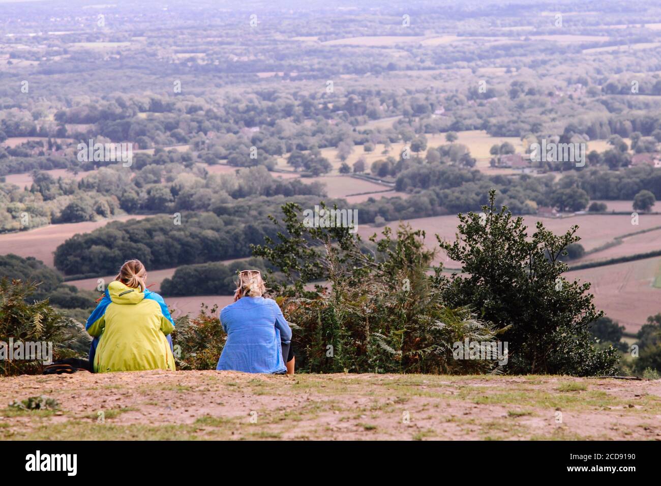 Two friends sit on a hill talking and looking out at Surrey Hills countryside from behind, England, UK, August 2020 Stock Photo