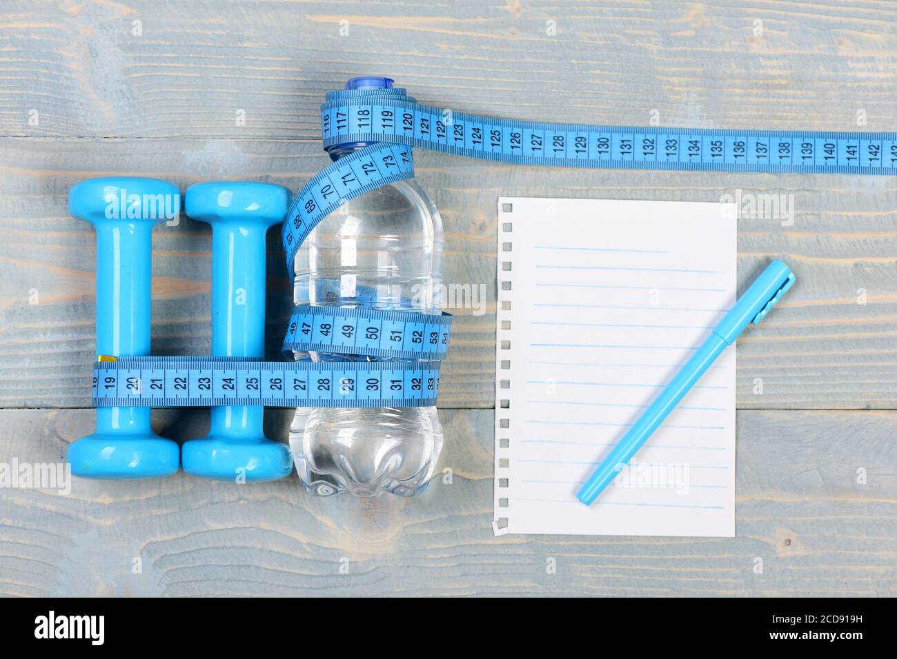 Centimeter tied around sports equipment in cyan blue on wooden vintage  background. Tools for healthy lifestyle. Workout and weight loss concept.  Bottle, apple, measuring tape and jump rope, top view Stock Photo 