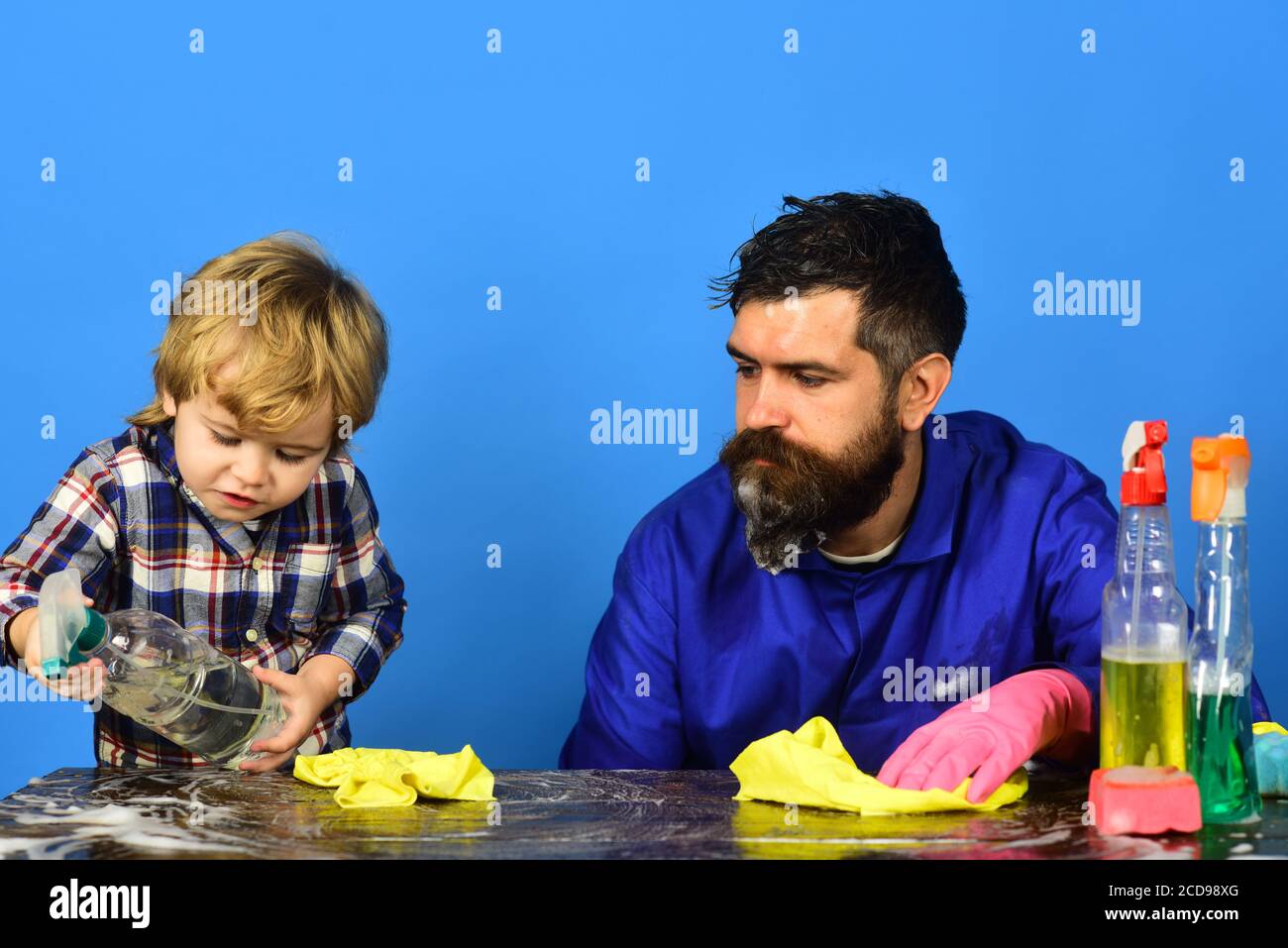 Dad with son and cleaning supplies on blue background. Kid holds spray ...