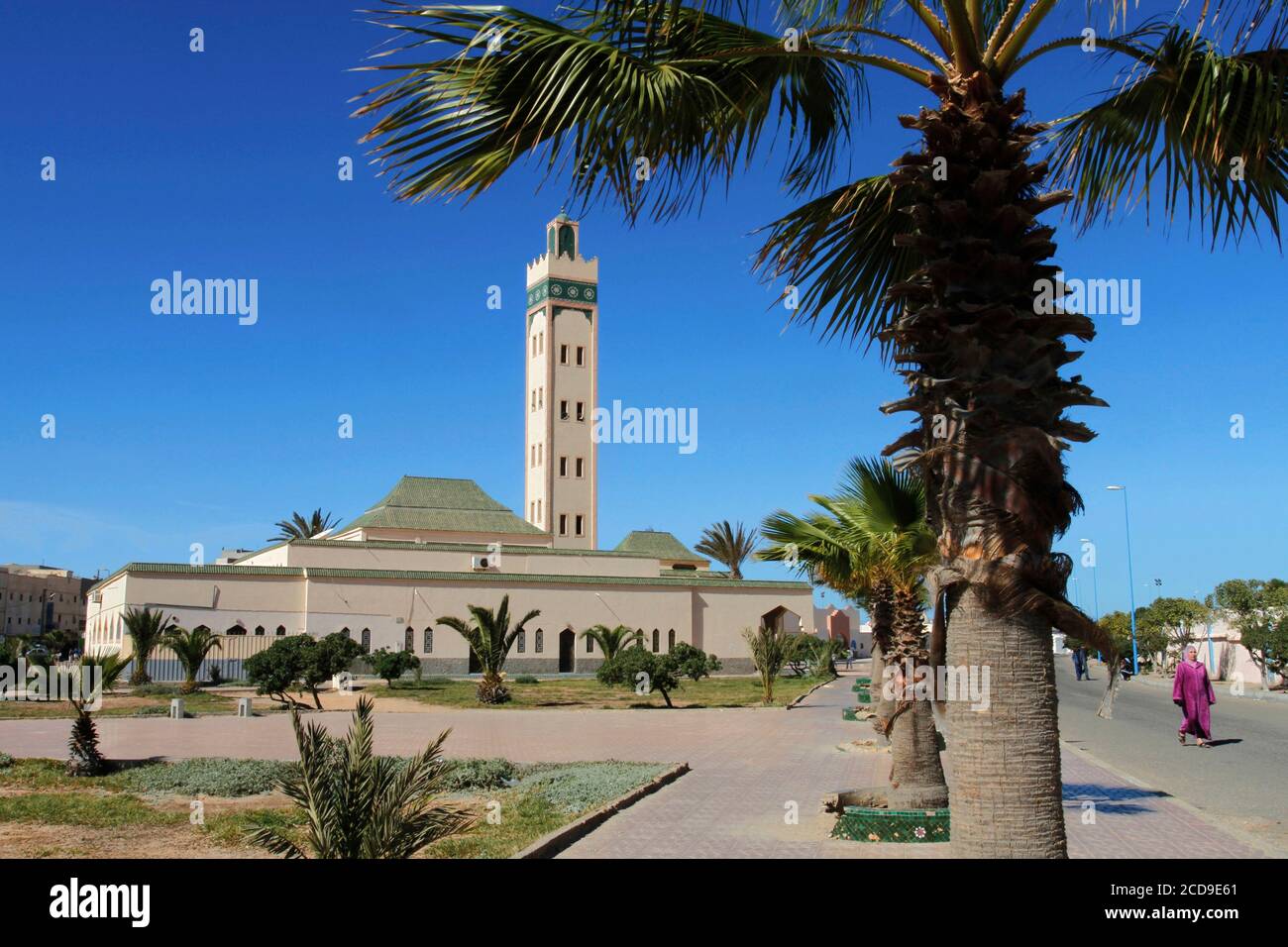 Morocco, Western Sahara, Dakhla, woman wearing traditional Saharawi clothing walking in front of Eddarham Mosque Stock Photo