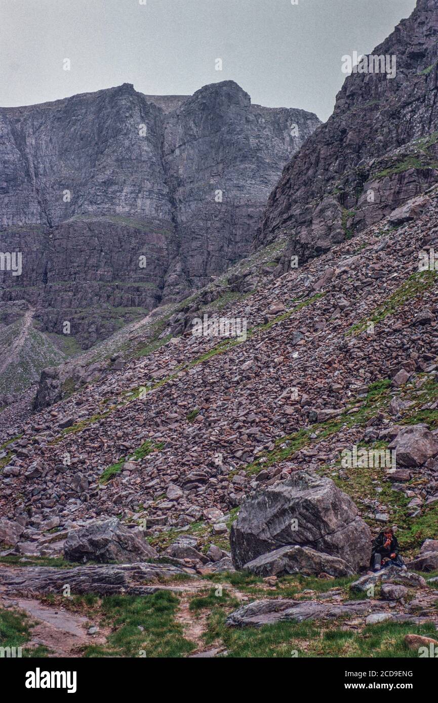 Hillwalker has lunch in the shelter of a boulder below, the triple buttresses of Coire Mhic Fhearchair, Ben Eighe, in Torridon, north west Scotland, archive image from 1990s Stock Photo