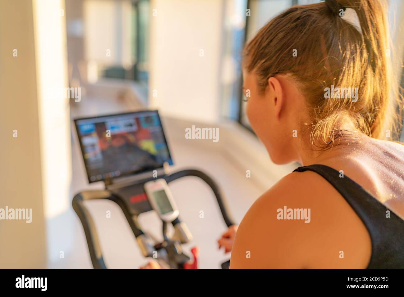 Fitness workout woman training at home on smart stationary bike equipment connected online live streaming class indoors for biking exercise. Indoor Stock Photo