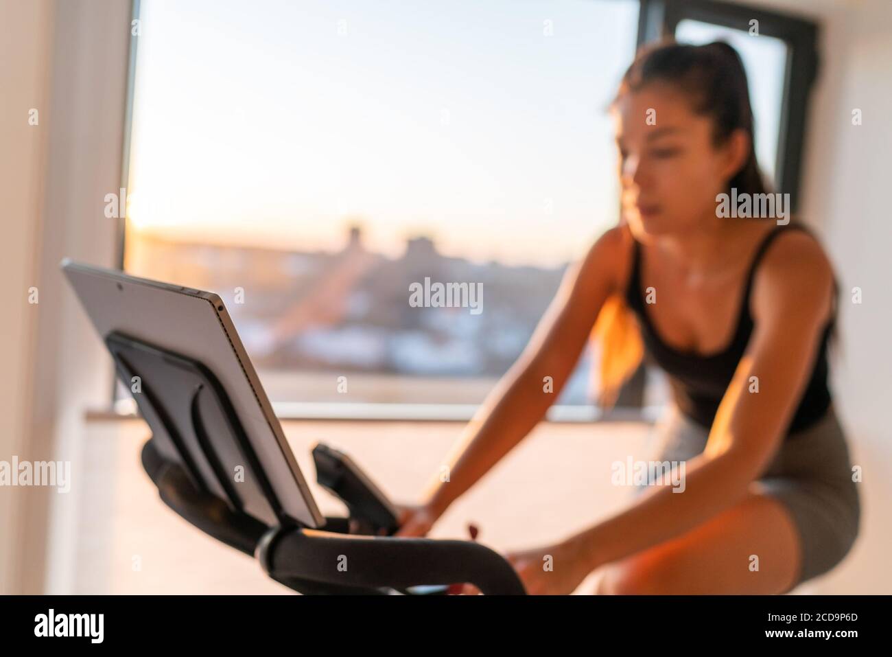 Home fitness fit woman exercising on smart stationary bike at home gym class watching screen online class biking exercise. Young girl training Stock Photo