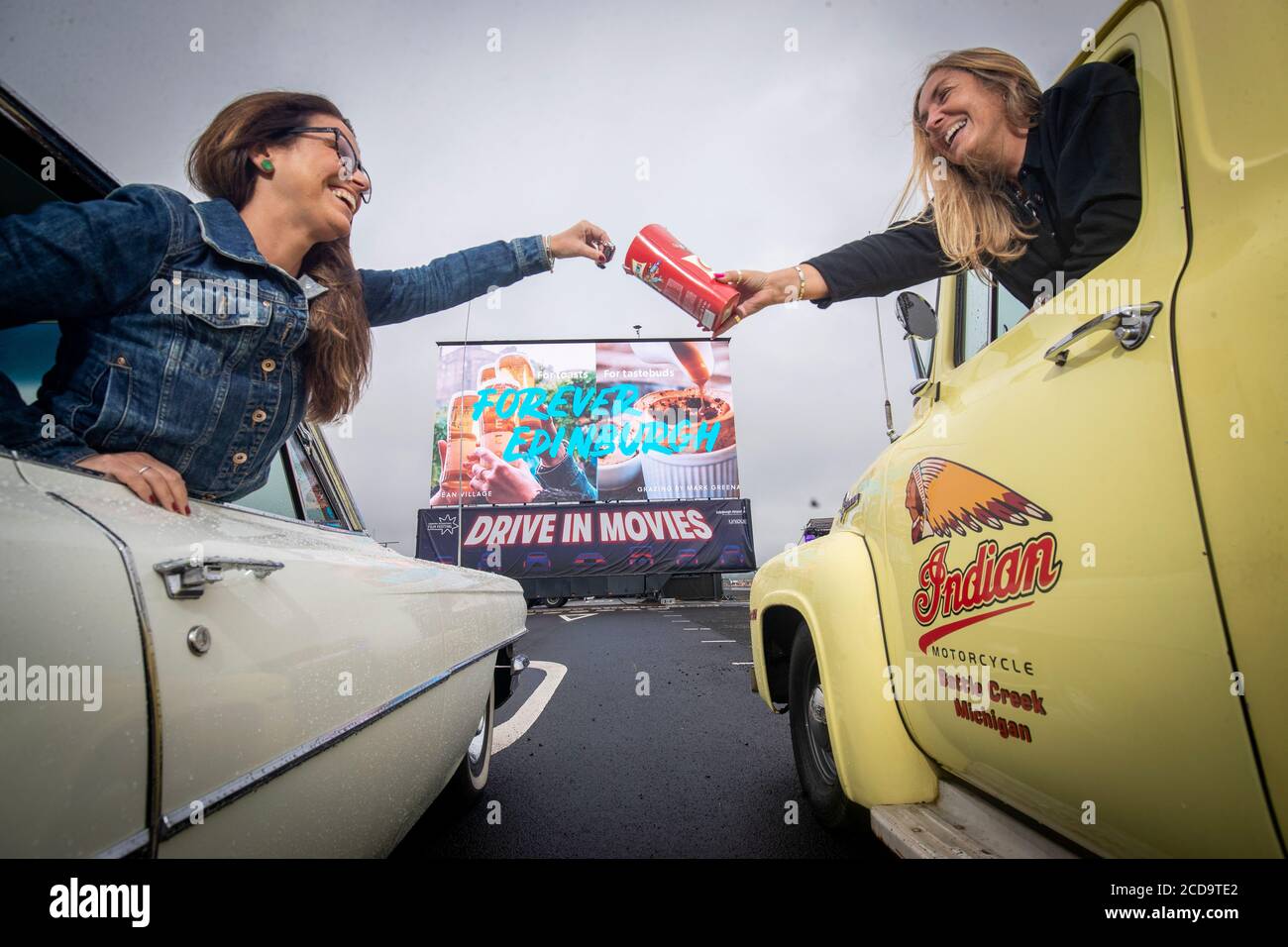 Movie-goers Ruth Wyatt (left) and Loraine Preston share sweets before watching the film Sunshine On Leith in their vintage cars at the socially distanced Drive-in Movie arena which has been set up at Edinburgh Airport as part of the Edinburgh International Film Festival. Stock Photo