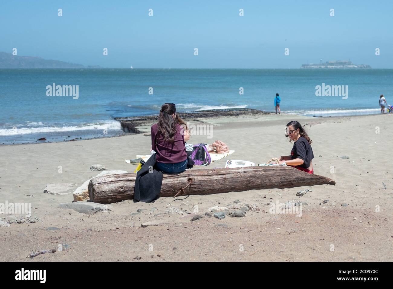 Young people sit on a piece of driftwood and enjoy a picnic on beach near Crissy Field, in the Presidio, San Francisco, California, June 28, 2020. () Stock Photo