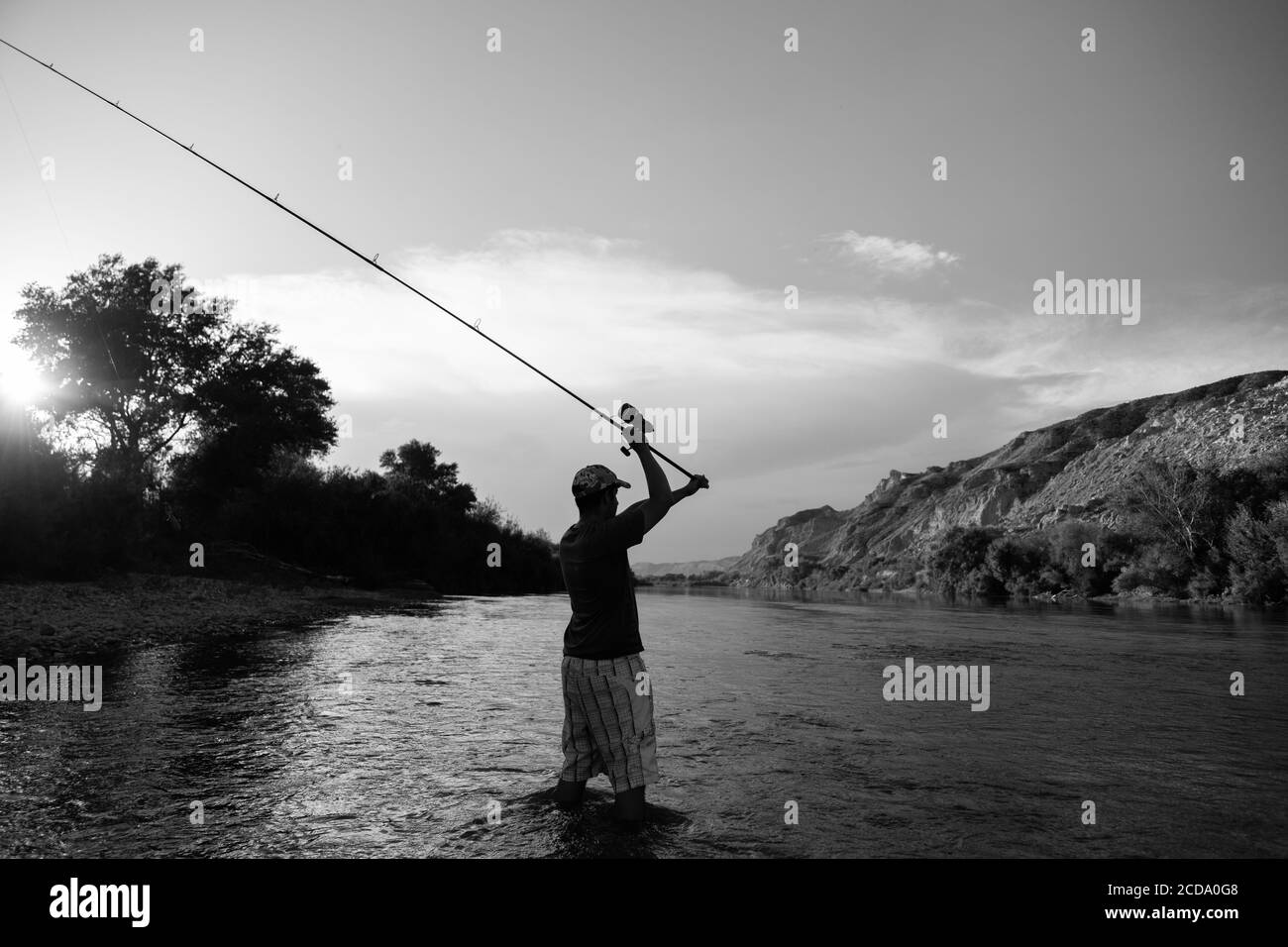 Greyscale shot of a male fishing in the river with a rod at sunset Stock Photo