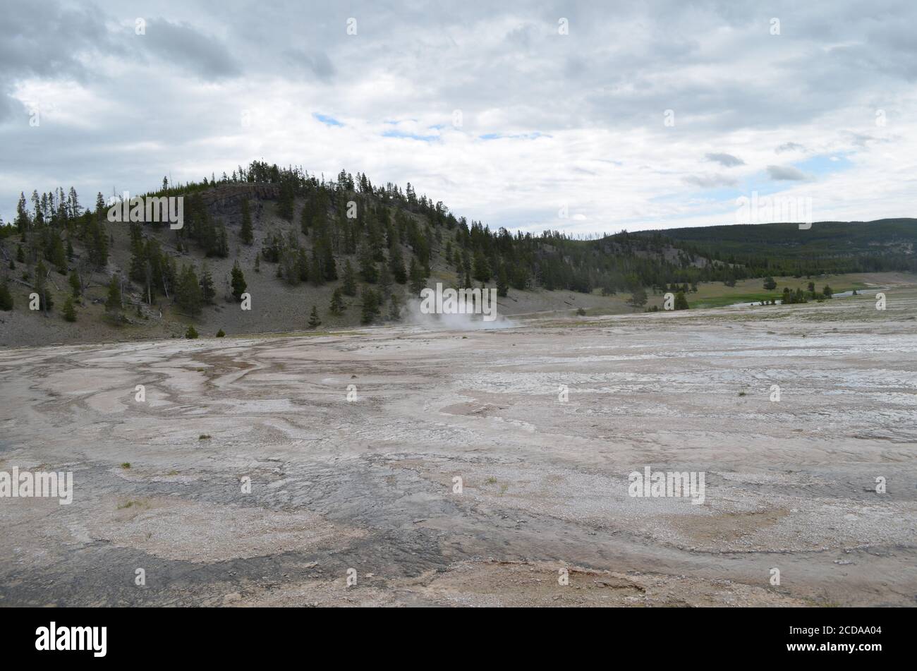 Late Spring in Yellowstone National Park: Indigo Spring of the Excelsior Group in Midway Geyser Basin with Firehole River and Midway Bluff Behind Stock Photo