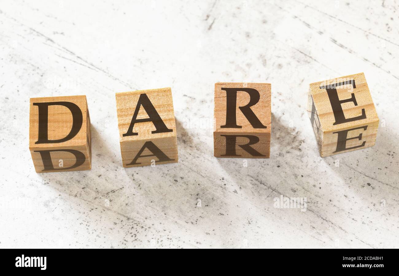 Four wooden cubes with letters DARE (stands for decision-making model -Define, Assess, Respond, Evaluate) on white working board. Stock Photo