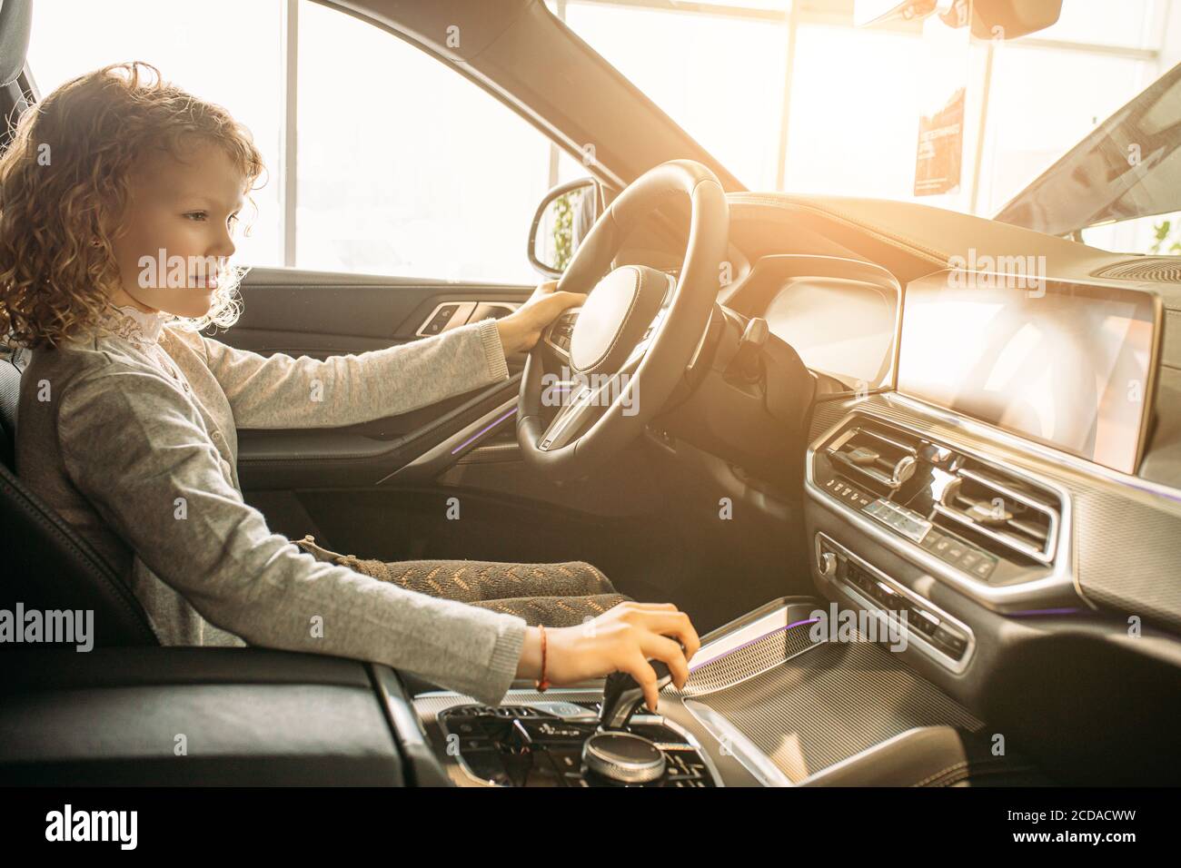 adorable young caucasian child girl want parents to buy this car, she sit at the wheel of new auto, girl likes it. in dealership Stock Photo
