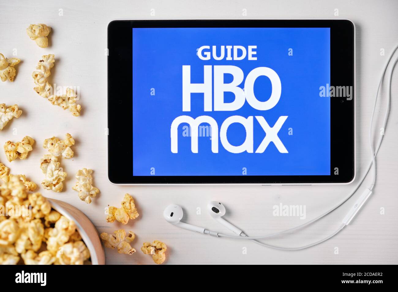 Guide HBO max logo on the screen of the tablet laying on the white table  and sprinkled popcorn on it. Apple earphones near the tablet showing a HBO  Stock Photo - Alamy